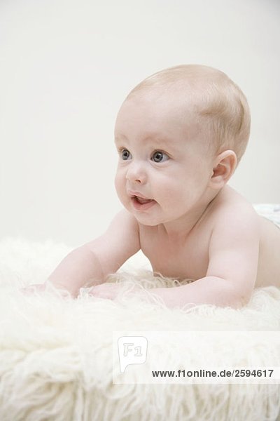 Ein Baby  das auf einem Schaffellteppich liegt.