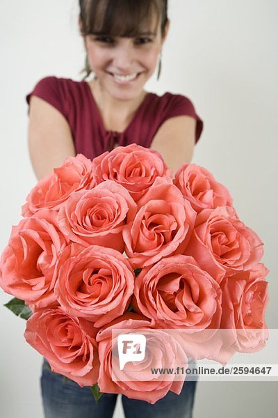 Eine lateinamerikanische Frau präsentiert einen Strauß Rosen.