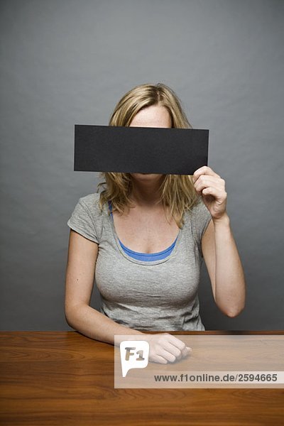 Eine junge Frau hält einen Zensurstreifen vor ihr Gesicht.