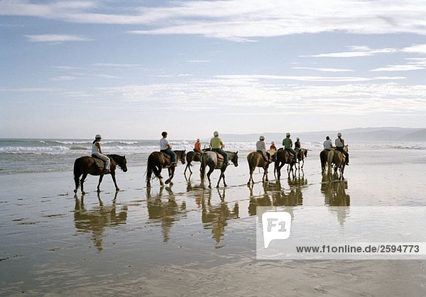 A group of people horseback riding on a beach