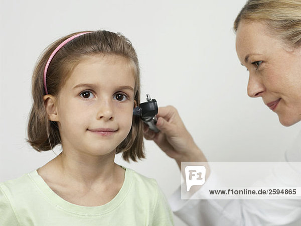 Eine Kinderärztin benutzt ein Otoskop  um das Ohr eines Mädchens zu untersuchen.