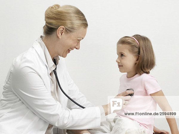 Eine Kinderärztin legt ein Stethoskop auf das Herz eines jungen Mädchens.
