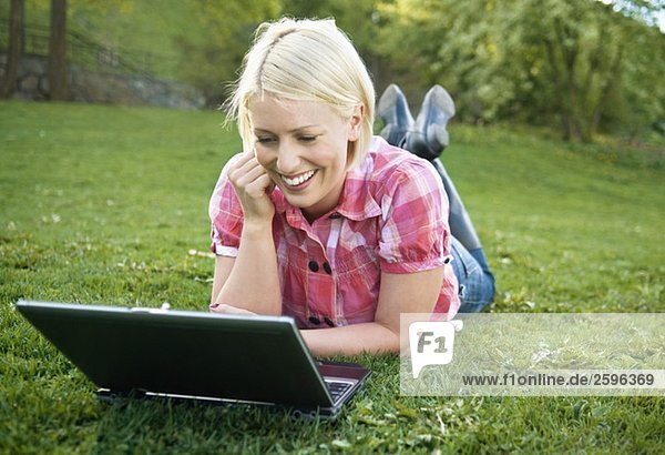 Girl lying in the grass looking at computer