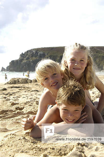 Portrait von drei Kindern am Strand liegen und lächelnd