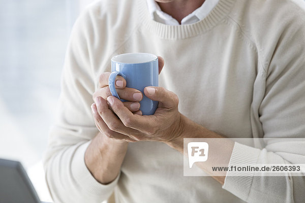 Senior trinkt ein warmes Getränk hält einen Becher in der Hand am Laptop