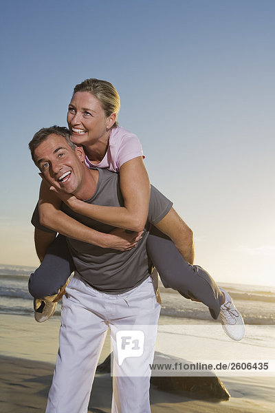 Senior couple having fun on beach man carrying woman piggyback