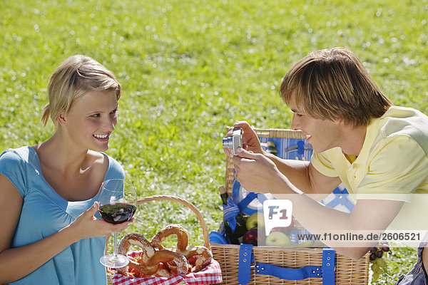 Young couple having picnic man taking photograph of woman