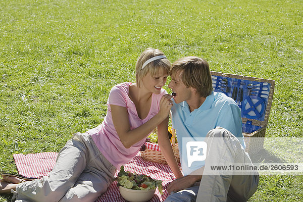 Junges Paar im Park beim Picknick mit Salat Frau füttert Mann