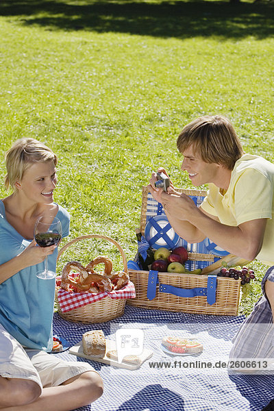 Young couple having picnic man taking photograph of woman
