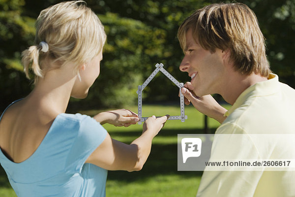 Junges Paar im Freien halten Meterstab in Form eines Hauses in der Hand