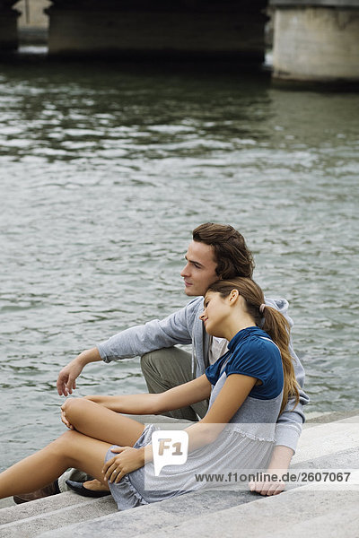 Young couple sitting on steps by river Seine Paris France