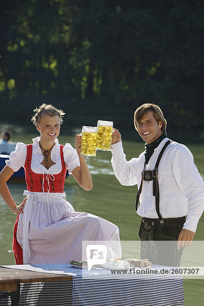 Junges Paar in Tracht steht am Biertisch prosten sich mit einer Maß Bier zu Biergarten am Seehaus Englischer Garten
