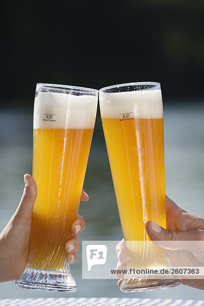 Junges Paar prosten sich mit Weizenbier zu Biergarten am Seehaus Englischer Garten Nahaufnahme der Gläser und Hände