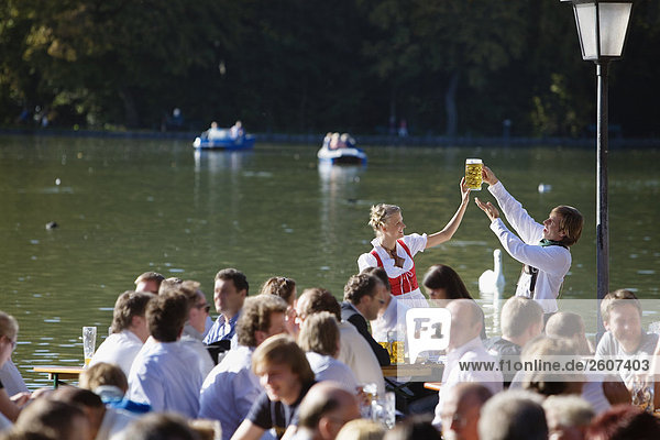 Junges Paar in Tracht steht im Biergarten am Seehaus Englischer Garten halten eine Mass Bier in der Hand Menschenmenge im Vordergrund