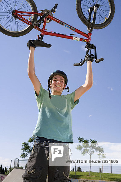 Jugendlicher Junge mit Fahrrad über dem Kopf