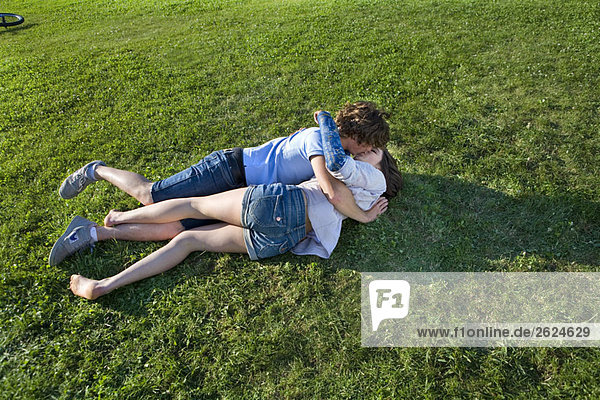 Teenagerpaar auf Gras liegend  küssend