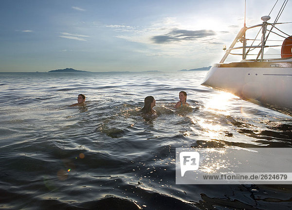Drei Personen schwimmen neben dem Segelboot