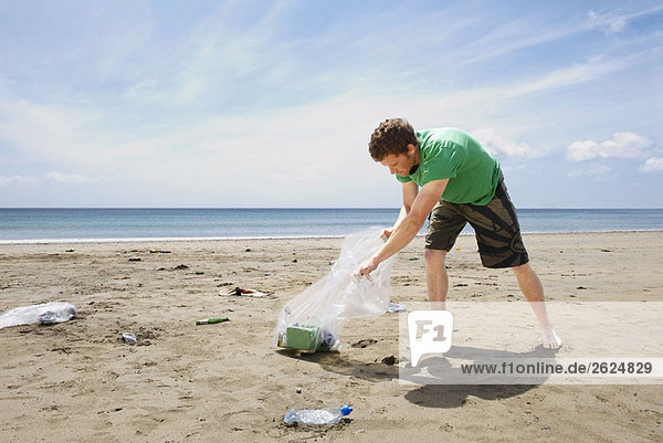 Junger Mann sammelt Müll am Strand
