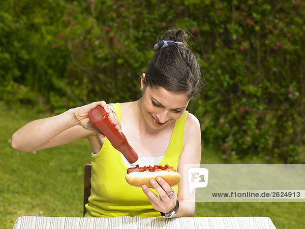 Junge Frau gießt Ketchup auf Hot Dog