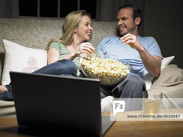 Young couple sharing popcorn on couch