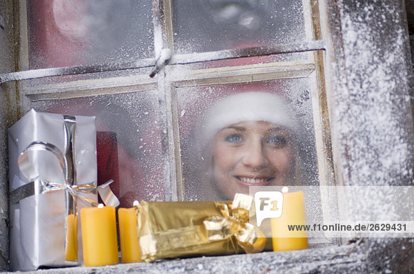 Austria  Salzburger Land  Young woman looking through window  parcels and candles on windowsill