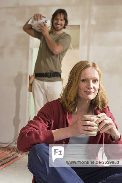 Young couple on construction site  woman holding cup