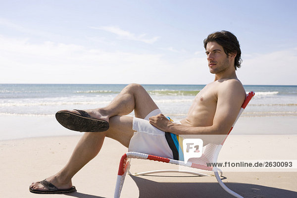 Germany  Baltic sea  Young man relaxing in chair on beach  portrait