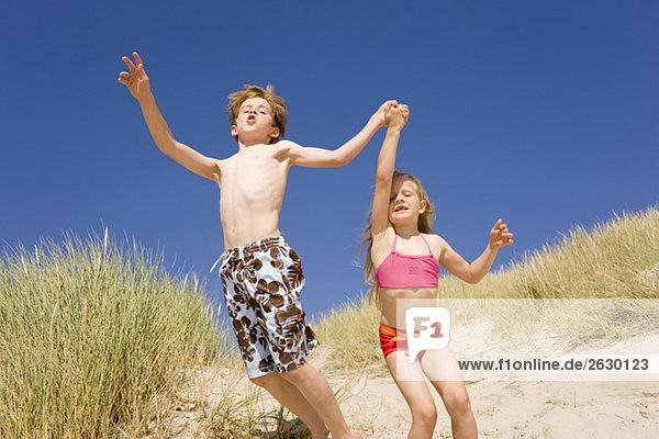 Deutschland  Ostsee  Junge (8-9) und Mädchen (6-7) springen die Stranddüne hinunter.