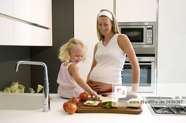 Pregnant mother and daughter (3-4) in the kitchen
