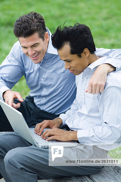 Geschäftspartner  die den Laptop gemeinsam im Freien benutzen  der eine Arm um die Schulter des anderen.