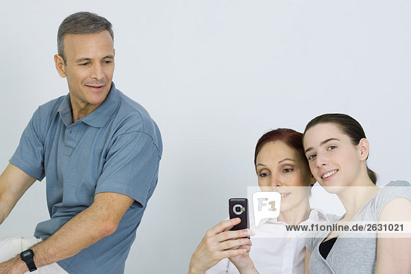 Familie sitzt zusammen  Eltern schauen aufs Handy  Tochter lächelt in die Kamera