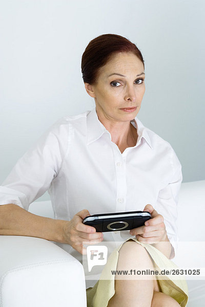 Reife Frau hält Handheld-Videospiel  Blick auf Kamera mit angehobener Augenbraue