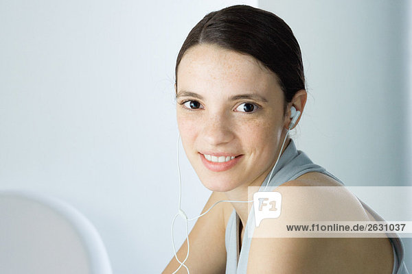 Young woman listening to earphones  smiling at camera