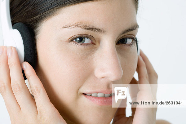 Woman listening to headphones  smiling at camera  close-up