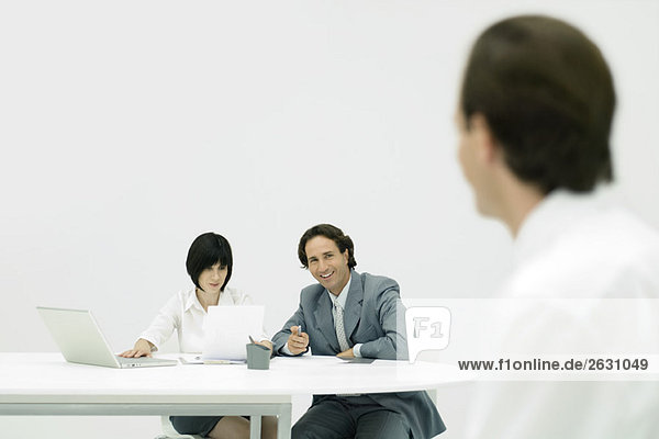 Professionals sitting at desk  woman reading document  man looking at person in foreground