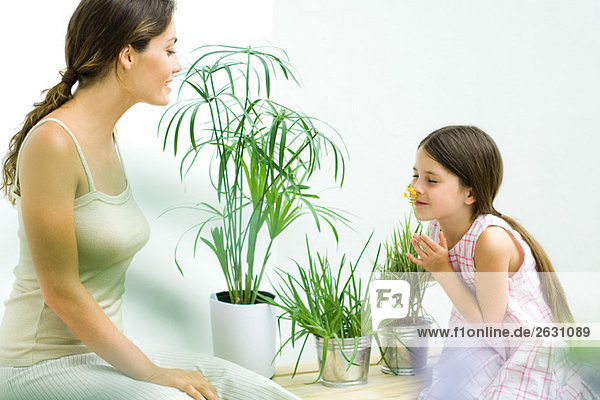 Mutter und Tochter sitzen mit Topfpflanzen  Mädchen riecht Blume  Augen geschlossen