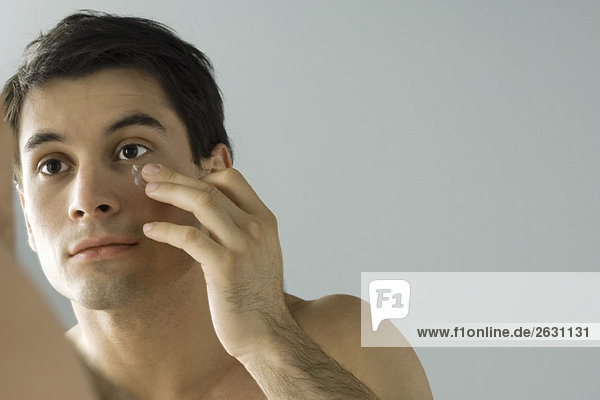 Man looking at himself in mirror  moisturizing face