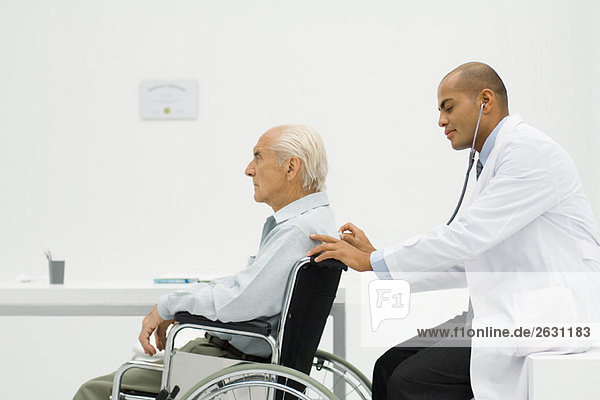 Elderly man sitting in wheelchair  doctor using stethoscope on back