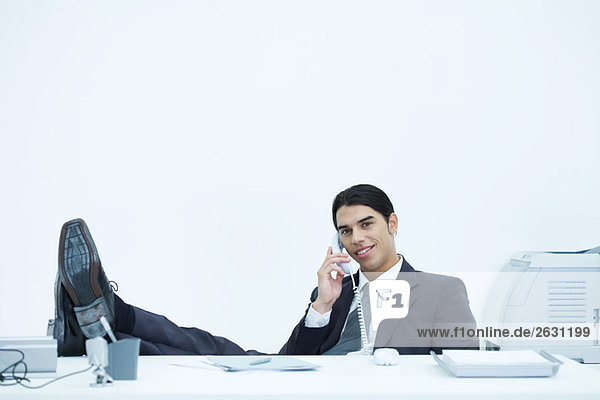 Young businessman sitting at desk with feet up  talking on landline phone