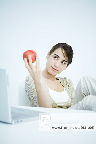 Young woman sitting at desk  looking at apple in hand