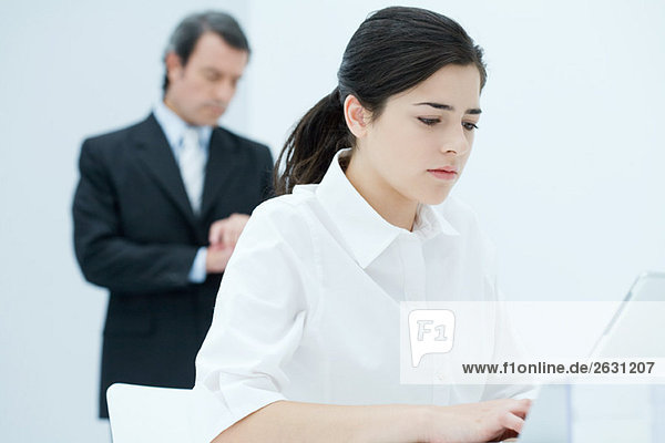 Junge Frau beim Tippen auf dem Laptop  Chef überprüft die Zeit im Hintergrund