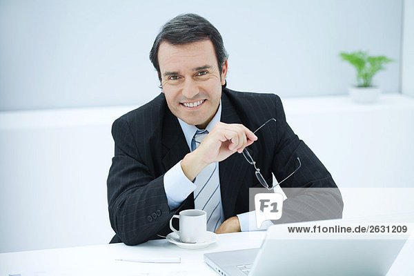 Geschäftsmann am Schreibtisch sitzend mit Kaffeetasse  lächelnd vor der Kamera