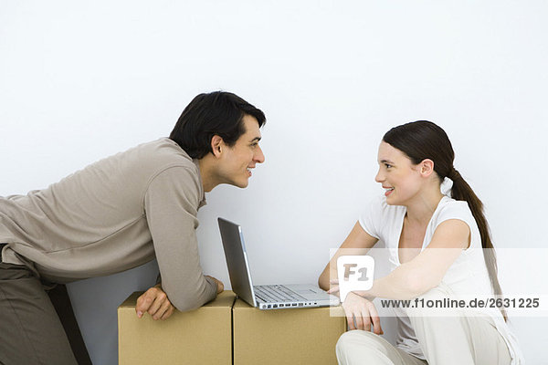 Couple sitting at makeshift desk with laptop computer between them  smiling at each other