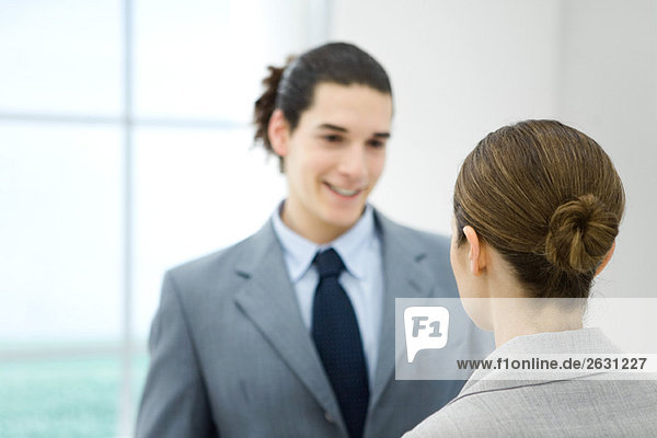 Professional young man facing female colleague  smiling