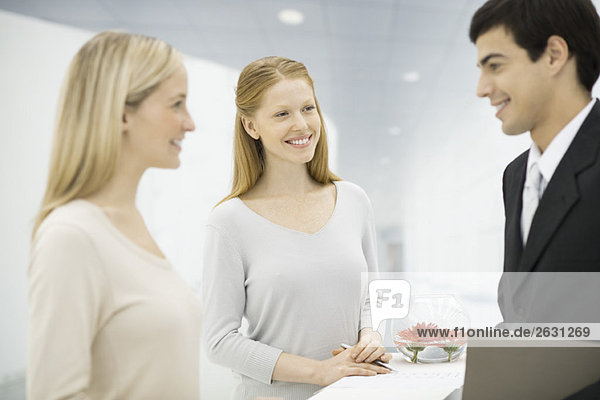 Businessman talking with two receptionists at counter  focus on women in center