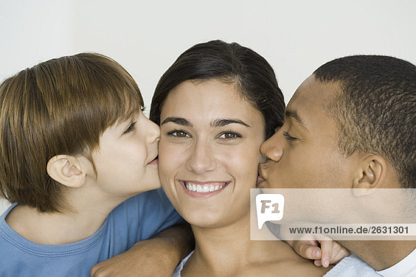 Husband and son kissing woman's cheeks  woman smiling at camera