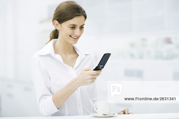 Woman standing at kitchen counter  looking at cell phone  smiling