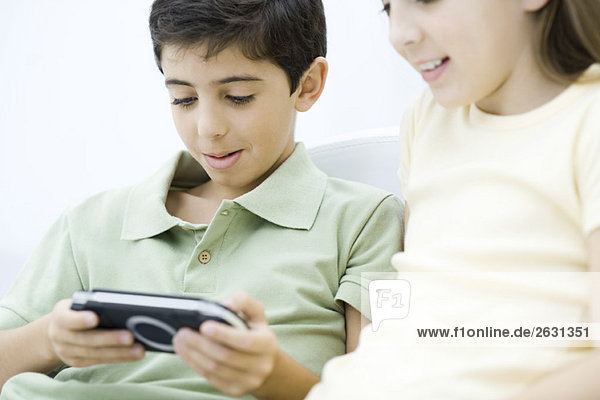 Brother and sister sitting together  boy playing handheld video game