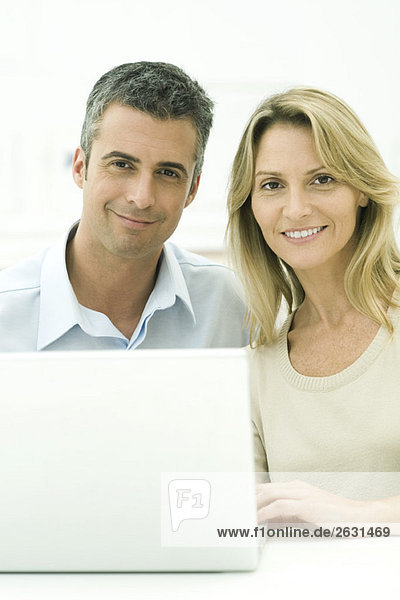 Couple sitting together with laptop  smiling at camera