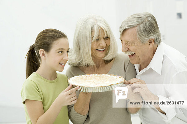 Großeltern und Enkelin lächeln sich an  die Frau hält Kuchen.